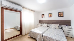 Une chambre avec un grand miroir, un lit avec une literie à motifs, une table de chevet et trois tableaux encadrés accrochés au mur.
