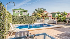 Une piscine avec une terrasse carrelée, une chaise et une plante en pot.