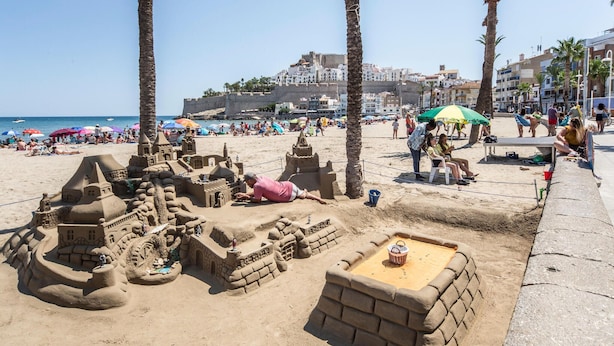 Une plage de sable avec un grand château de sable et des palmiers.