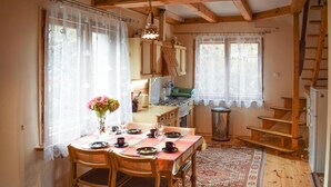 Une cuisine chaleureuse avec des meubles en bois, une table à manger pour quatre personnes et un escalier menant à l’étage supérieur.