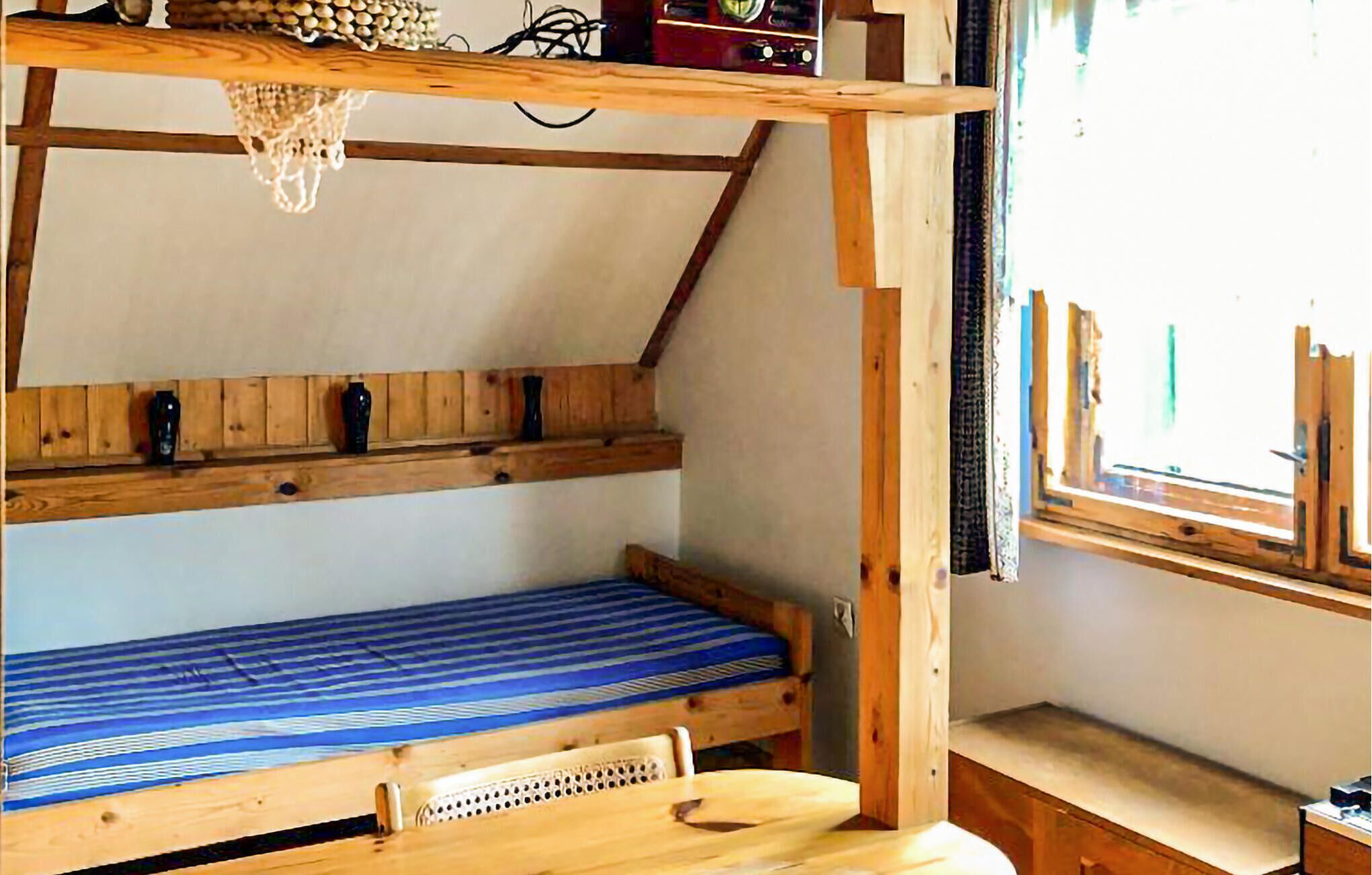 A wooden bunk bed with a blue mattress, a small wooden table, and a window with curtains.