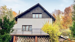 Une maison à deux étages avec un balcon, entourée d’arbres et d’une clôture en bois.