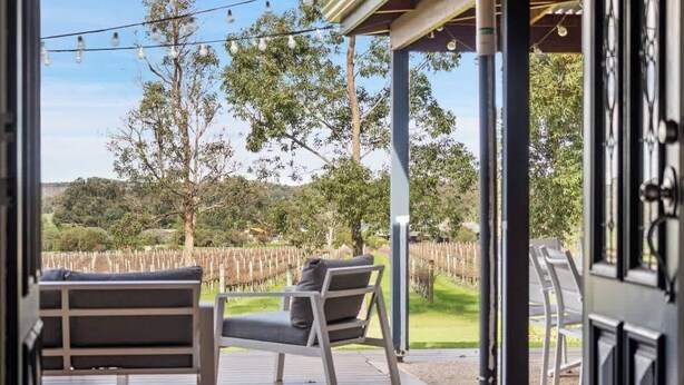 Un patio abierto con dos sillas y una mesa, una pérgola y un viñedo al fondo.