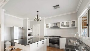 A modern kitchen with white cabinetry, a central island, stainless steel appliances, and a bar stool. - Burton Farmhouse Reconnect with Nature and Family (Wilyabrup)