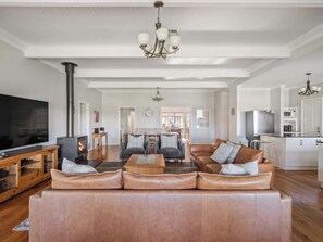 A spacious living room with a large leather sofa, a television, a fireplace, and a chandelier. - Burton Farmhouse Reconnect with Nature and Family (Wilyabrup)
