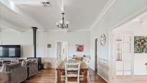 Amplia sala de estar con una mesa de comedor de madera, sillas blancas, un conjunto de sofás, una chimenea y un televisor.