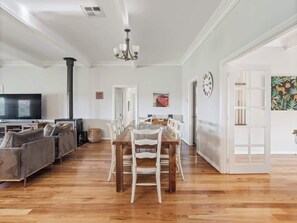 A spacious living area with a wooden dining table, white chairs, a sofa set, a fireplace, and a television. - Burton Farmhouse Reconnect with Nature and Family (Wilyabrup)