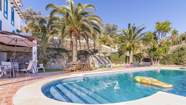A swimming pool with a tiled edge, surrounded by palm trees and a stone wall. - Cozy home in Mijas Pueblo with private swimming pool, can be inside or outside (Mijas Pueblo)