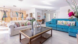 A spacious living room with a white sofa, a blue sofa, and a glass coffee table. There are decorative pillows and a vase with flowers on the blue sofa. - Cozy home in Mijas Pueblo with private swimming pool, can be inside or outside (Mijas Pueblo)