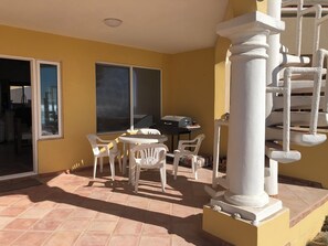 A balcony with a table and chairs, a grill, and a view of the city.