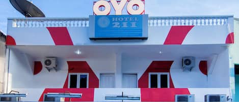 A hotel building with a prominent sign reading 'OYO HOTEL 211' and a satellite dish on the roof.