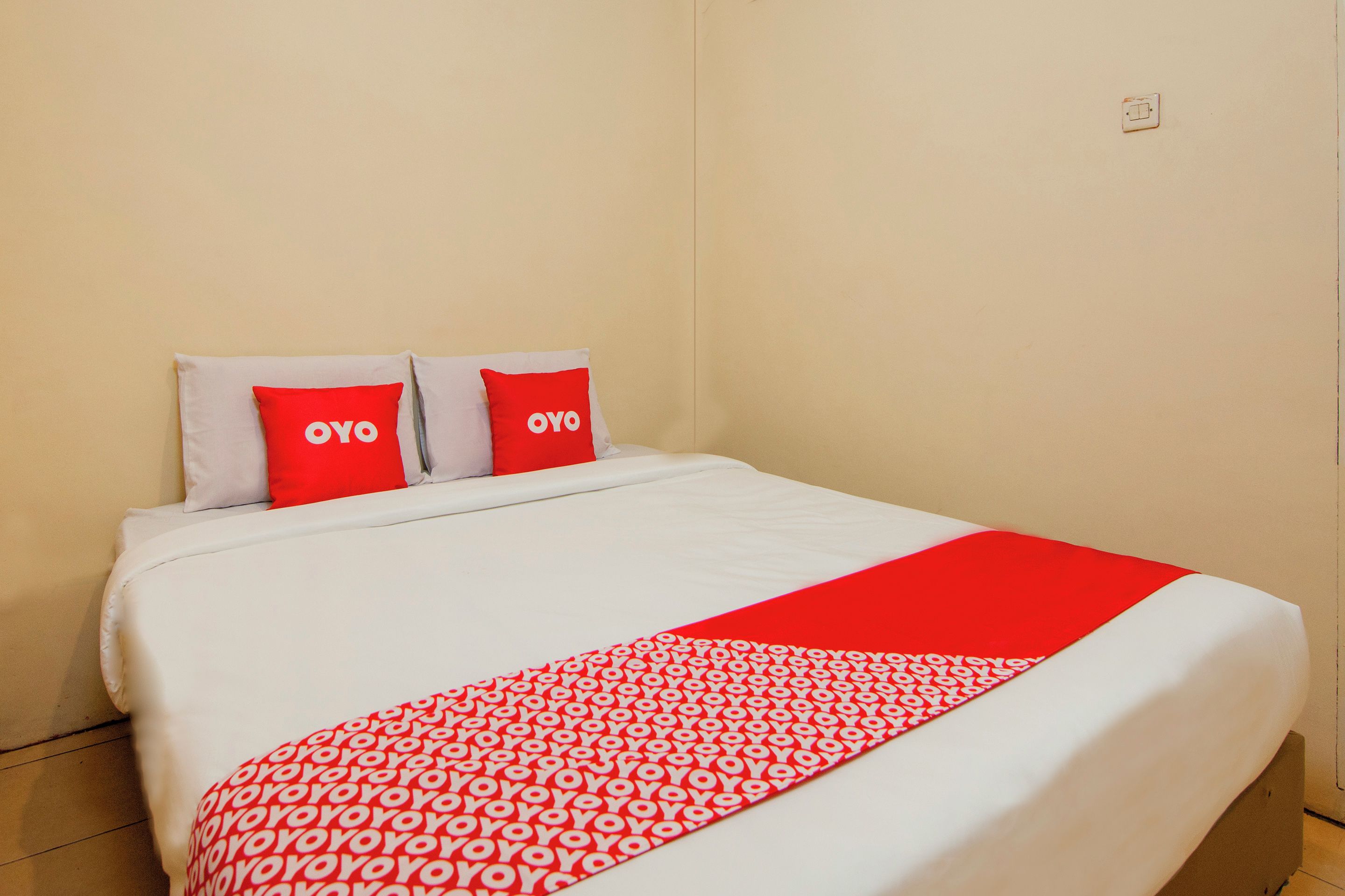 A hotel room with a bed, two pillows with the word 'OYO' on them, and a red and white patterned throw blanket.
