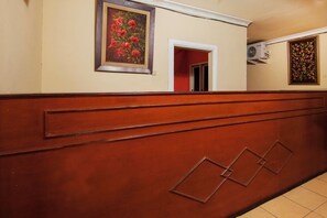 A hallway with a wooden panel, a framed floral painting, and a Samsung air conditioning unit. - OYO 2045 Hotel 211 (Parapat)