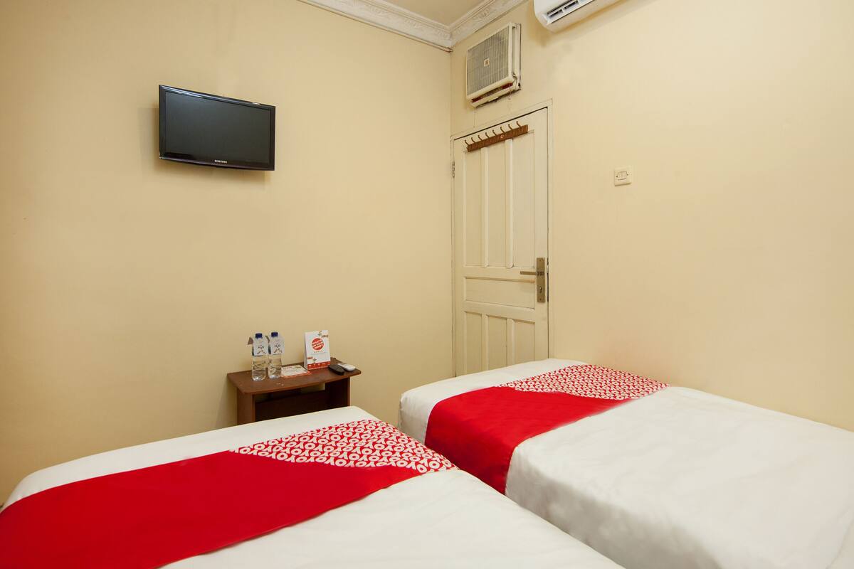 Quarto de hotel com duas camas, uma televisão, uma mesinha com garrafas de água e uma porta.