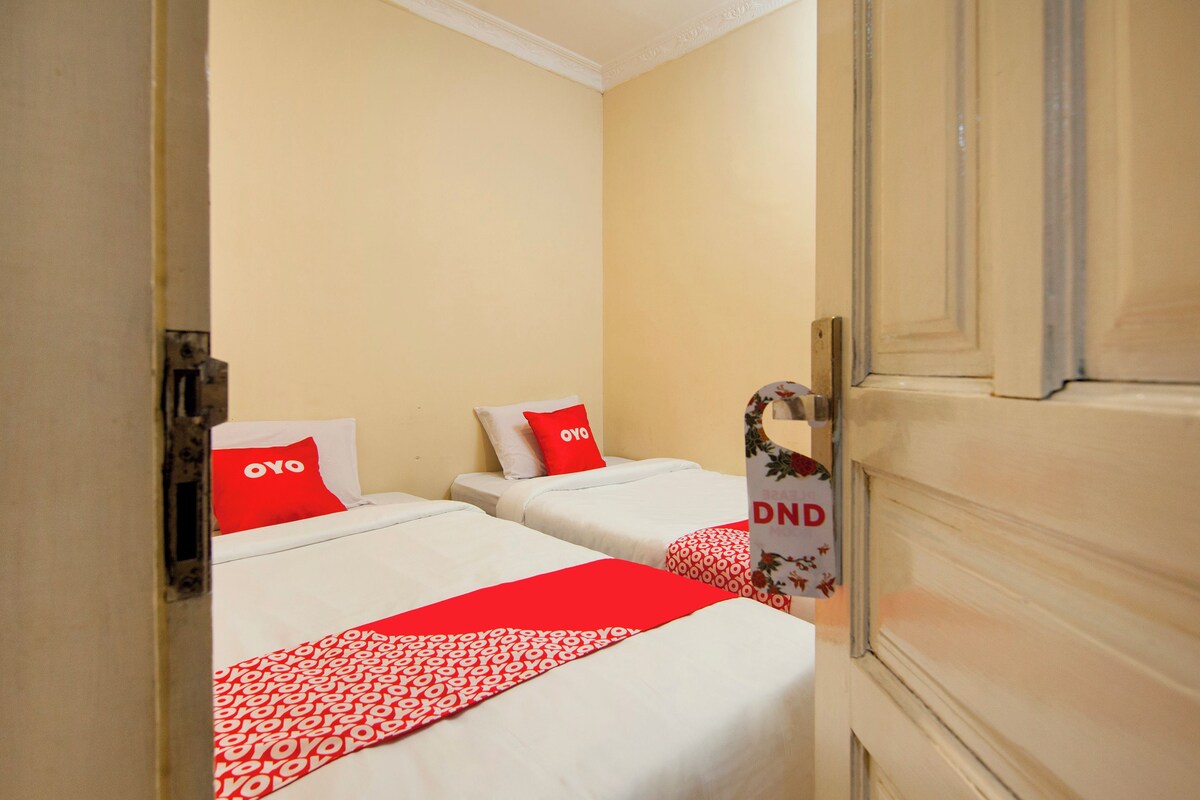 Quarto de hotel com duas camas, cada uma com colcha e almofadas vermelhas e brancas, e uma porta com padrão floral.