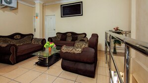A living room with two sofas, a coffee table, and a TV mounted on the wall. - OYO 2045 Hotel 211 (Parapat)