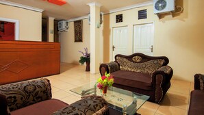 A living room with a sofa, a coffee table with a vase, and a door in the background. - OYO 2045 Hotel 211 (Parapat)