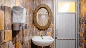 Une salle de bain avec un mur recouvert de carreaux de pierre, un lavabo blanc et un miroir rond doté d’un cadre en bois.