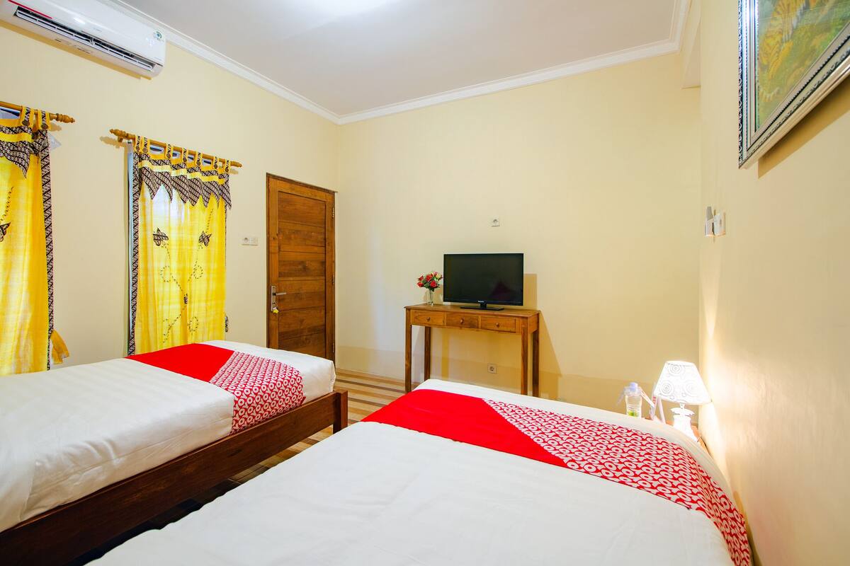 Habitación de hotel con dos camas, un televisor sobre una mesita y una puerta.