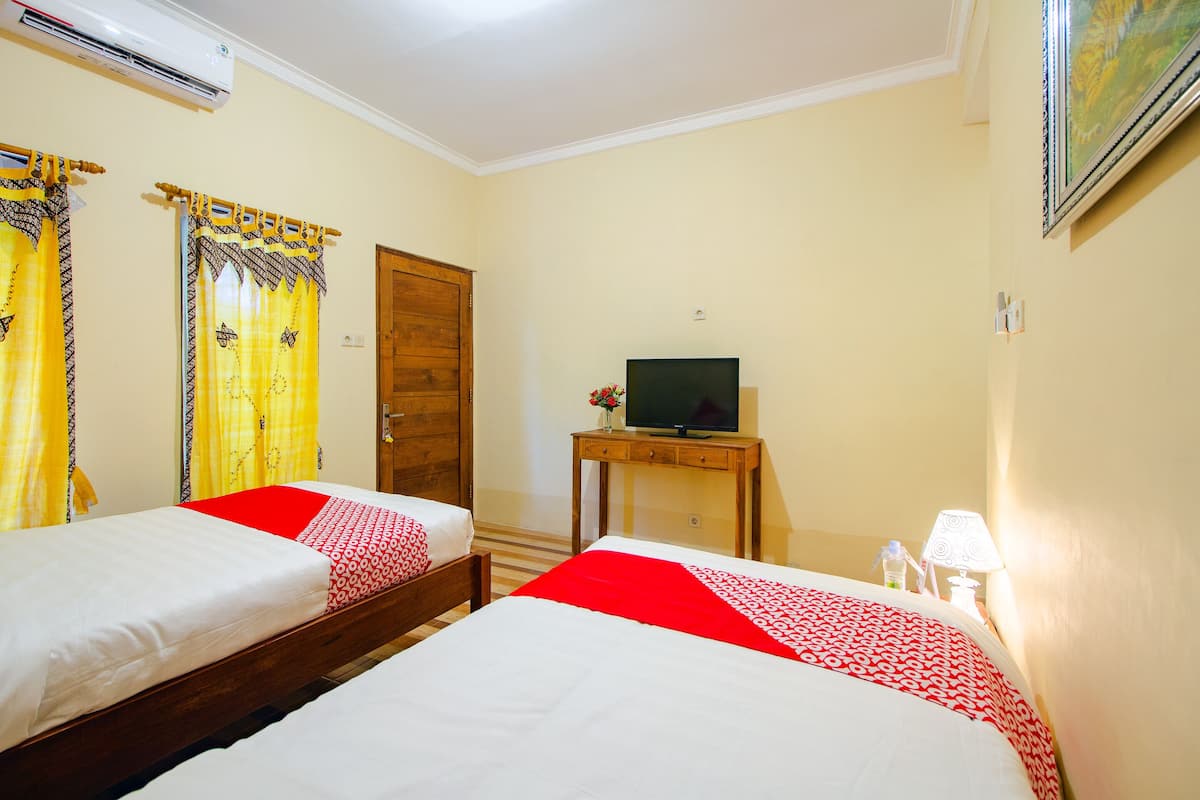A hotel room with two beds, a television on a wooden table, and a door.