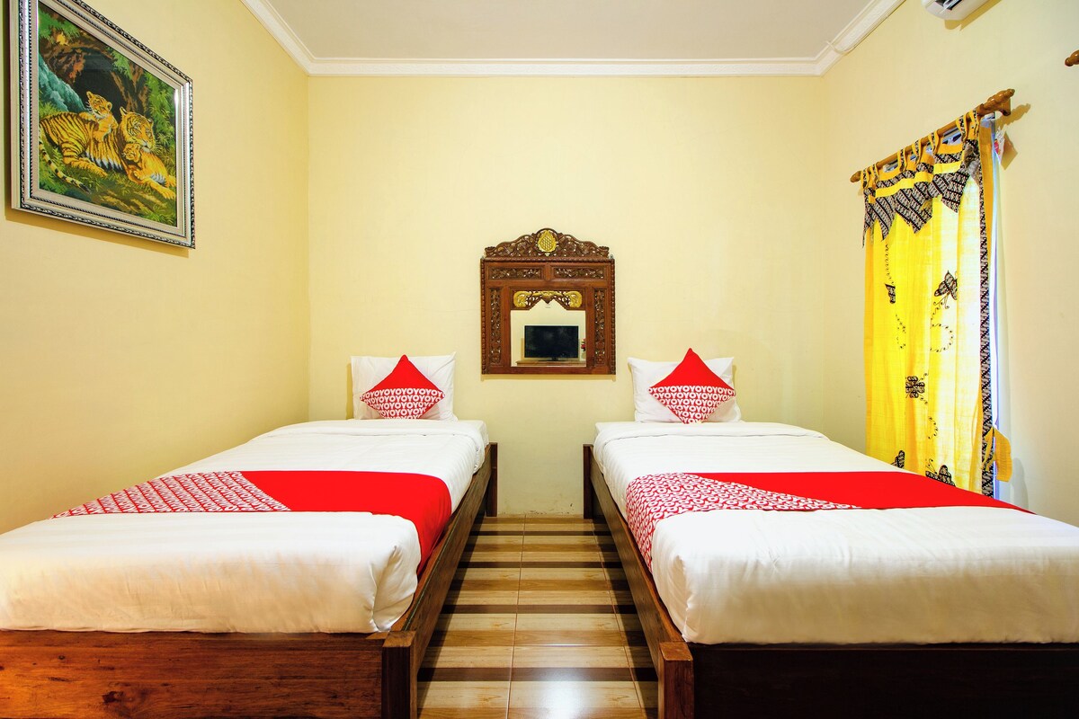 Ein Hotelzimmer mit zwei Einzelbetten, Holzboden, einem gerahmten Bild an der Wand und einem Spiegel über den Betten.