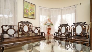 A traditional dining room with ornate wooden furniture, a glass-top table, and a floral arrangement on a side table.