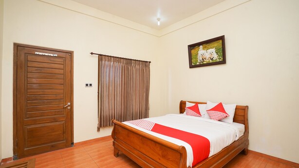 A bedroom with a wooden bed, a door, a window with curtains, and a wall-mounted picture.