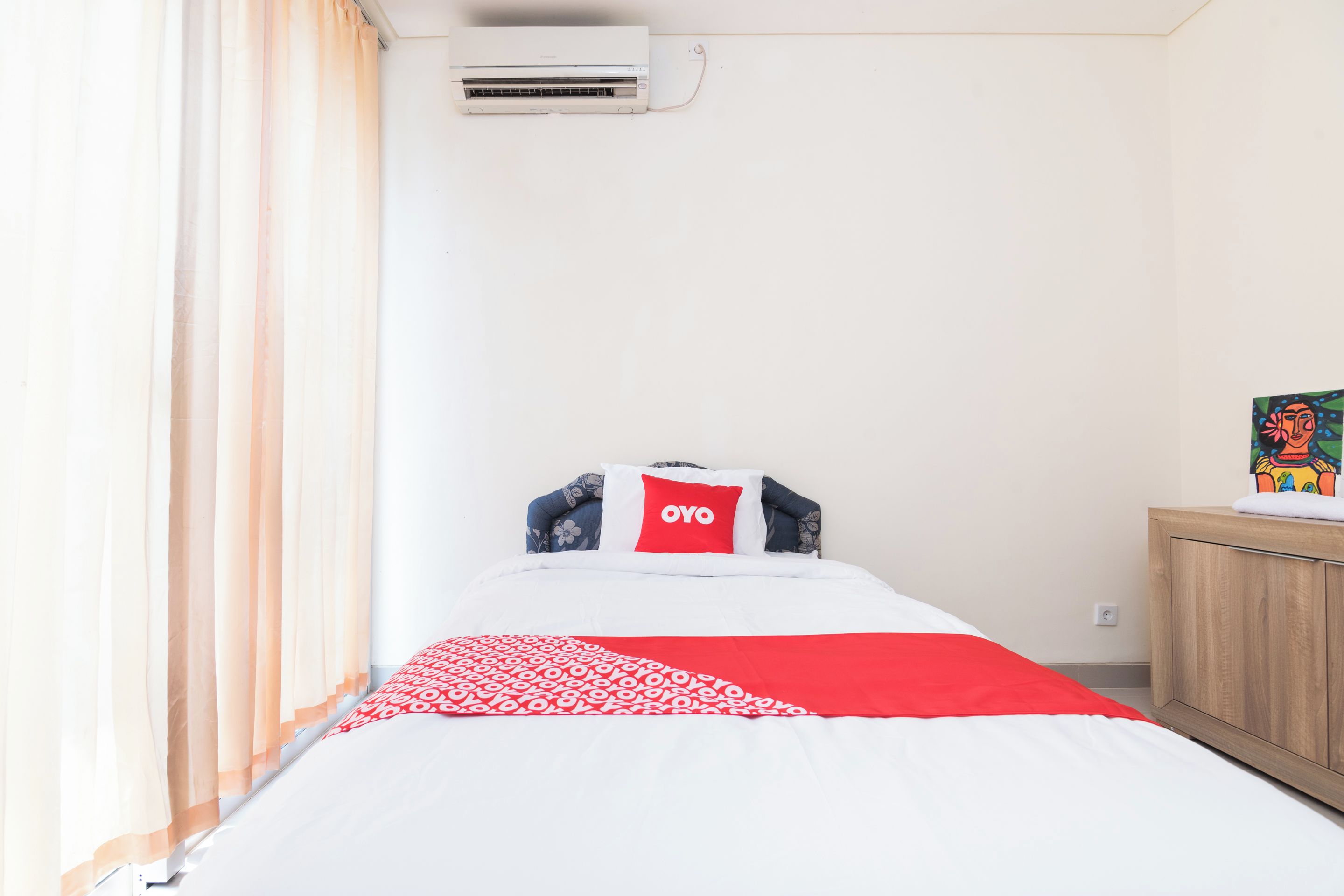 A bedroom with a bed, a pillow with the word 'YOYO', a window with curtains, and a wall-mounted air conditioner.