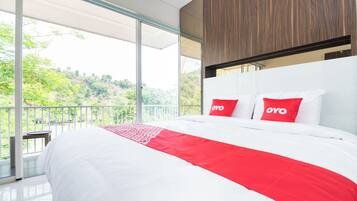 Una camera d'albergo moderna con un letto grande, due cuscini rossi con il marchio 'OYO', un balcone vista verde e una parete d'accento in legno.