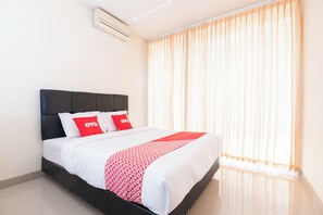 A hotel room with a bed, a headboard, a window with curtains, and an air conditioning unit. - OYO 2001 Taman Dayu Villa Golf View (Prigen)
