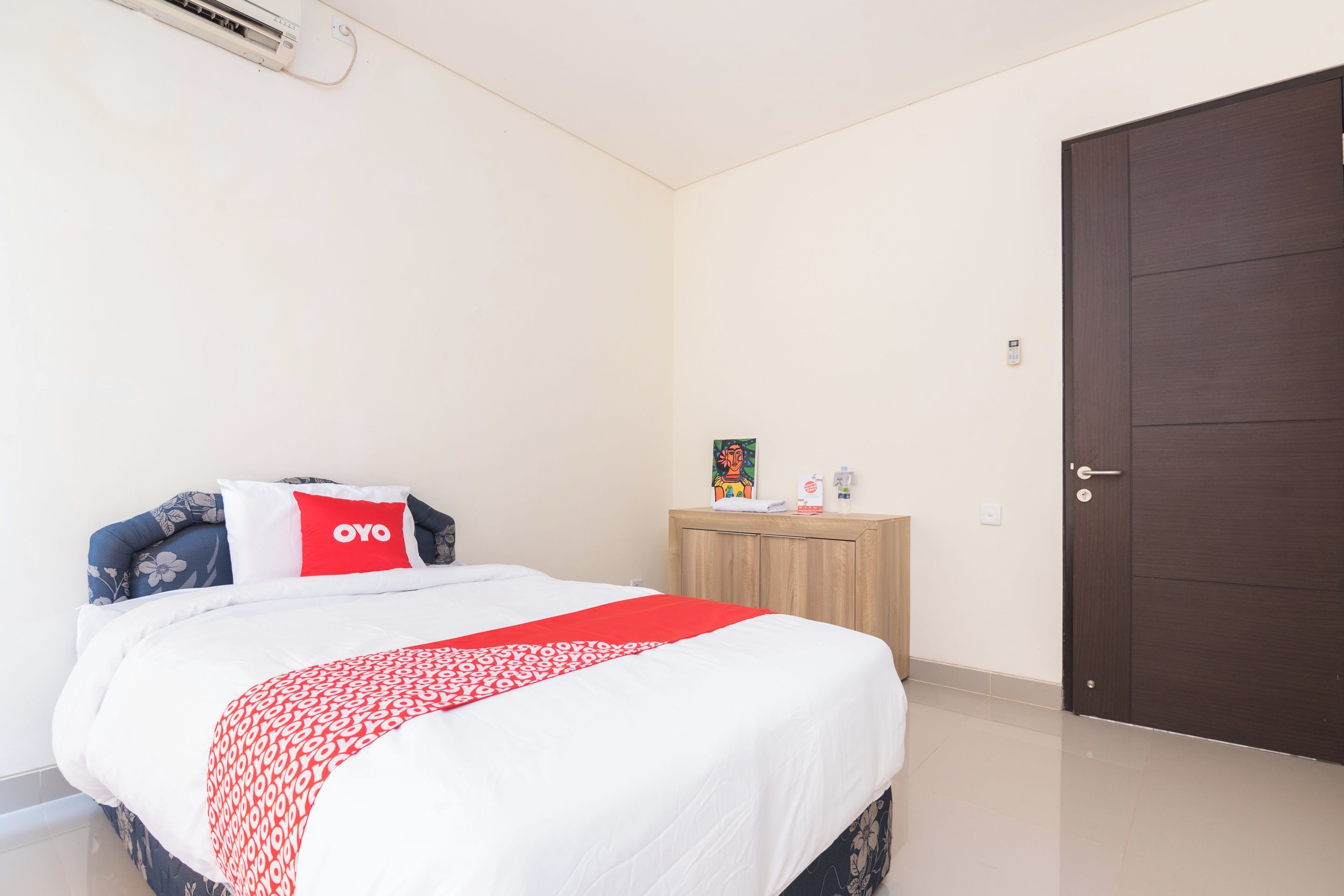 Una camera d'albergo con un letto, un comodino in legno, una porta e un climatizzatore a muro.