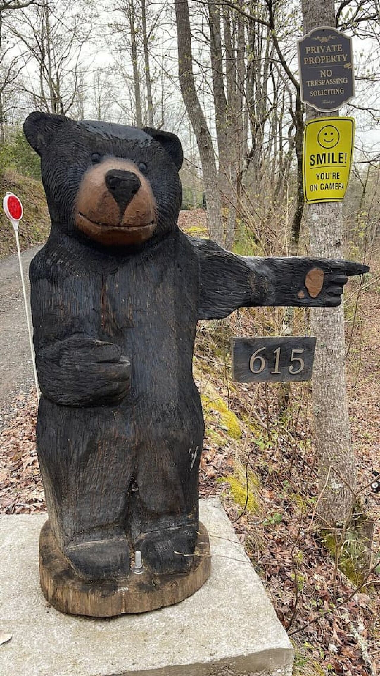 Eine hölzerne Bärenstatue mit einem Schild, auf dem '615' steht, und einem Schild mit der Aufschrift 'lächeln, Sie werden gefilmt'.