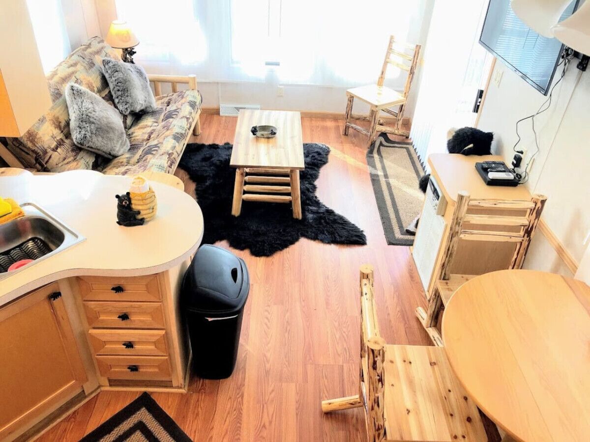 Un espacio habitable compacto con kitchenette, un sofá con cojines, una mesa de comedor y un televisor montado en la pared.