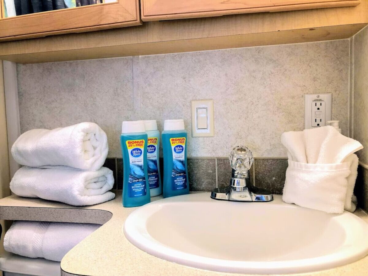 Un baño con un lavamanos, tres botellas de gel de baño y toallas.