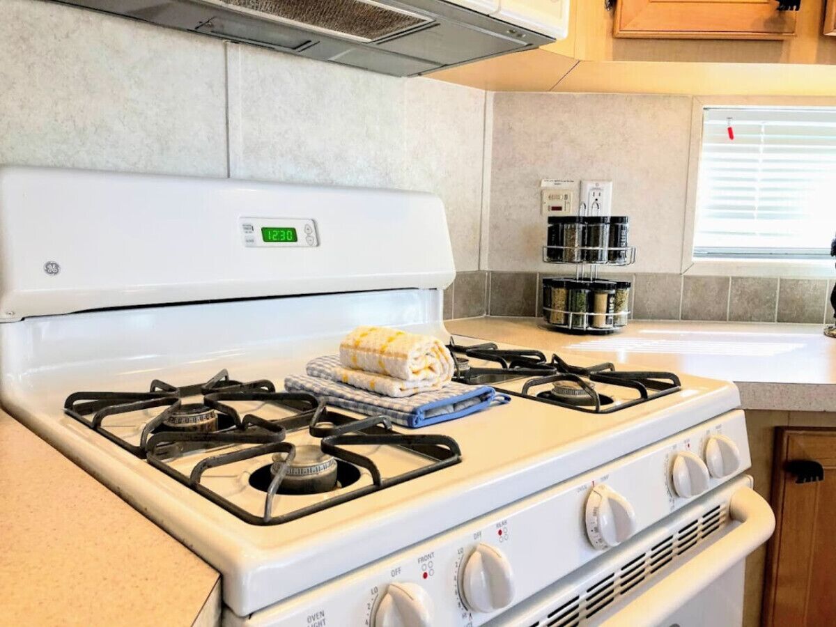 Una cocina con estufa blanca, un reloj digital y una ventana con persianas.