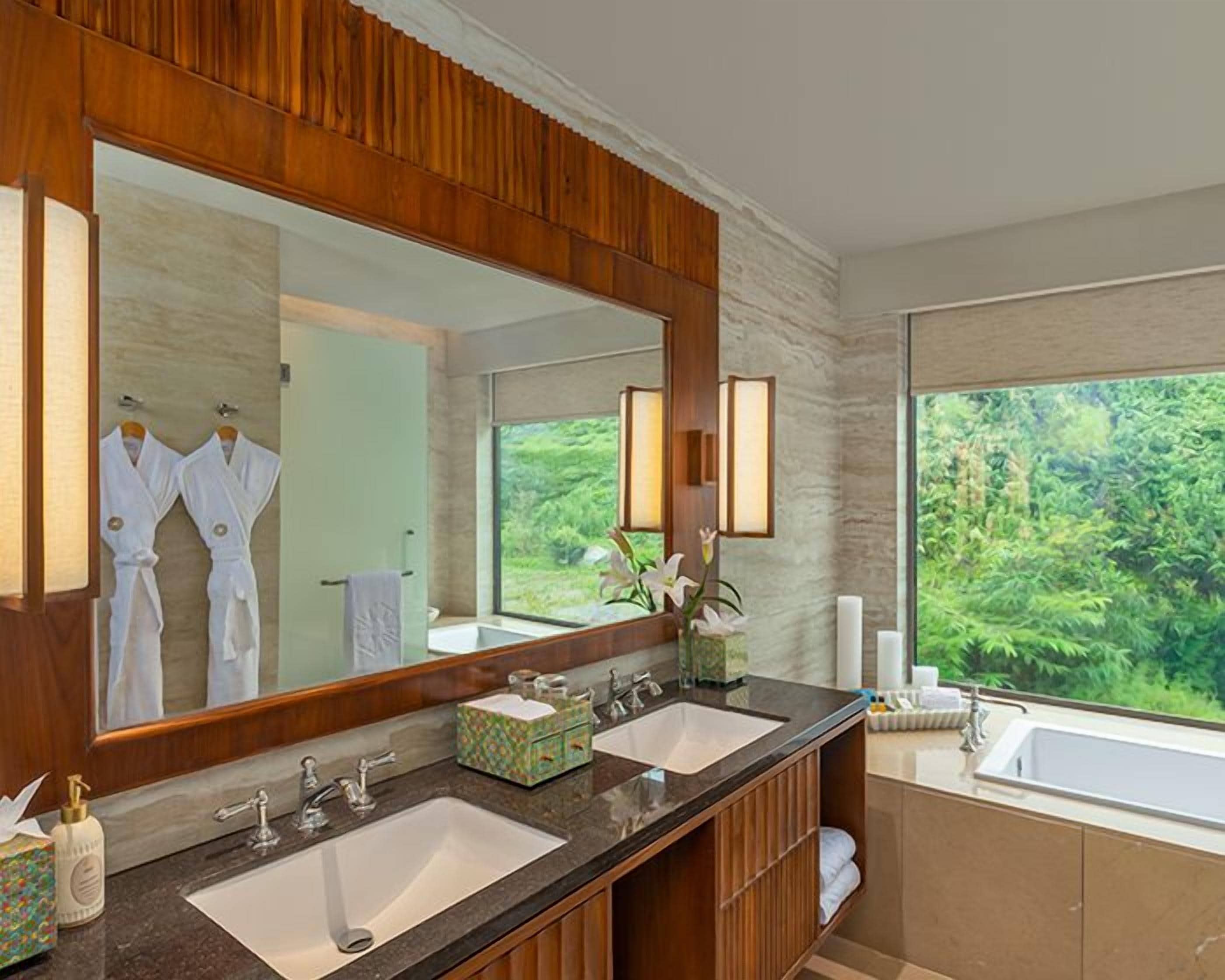 A bathroom with two sinks, a large mirror, and a view of greenery outside.