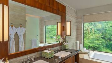Une salle de bain avec deux lavabos, un grand miroir et une vue sur la verdure à l’extérieur.