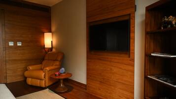 Una habitación con pared de madera, un sillón de cuero, una mesita redonda con una lámpara y un televisor montado en la pared.