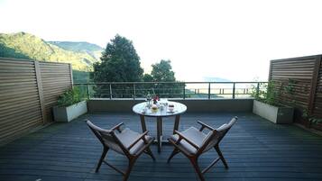 Une table ronde entourée de chaises, placée sur une terrasse en bois, d’où l’on peut admirer un paysage montagneux.
