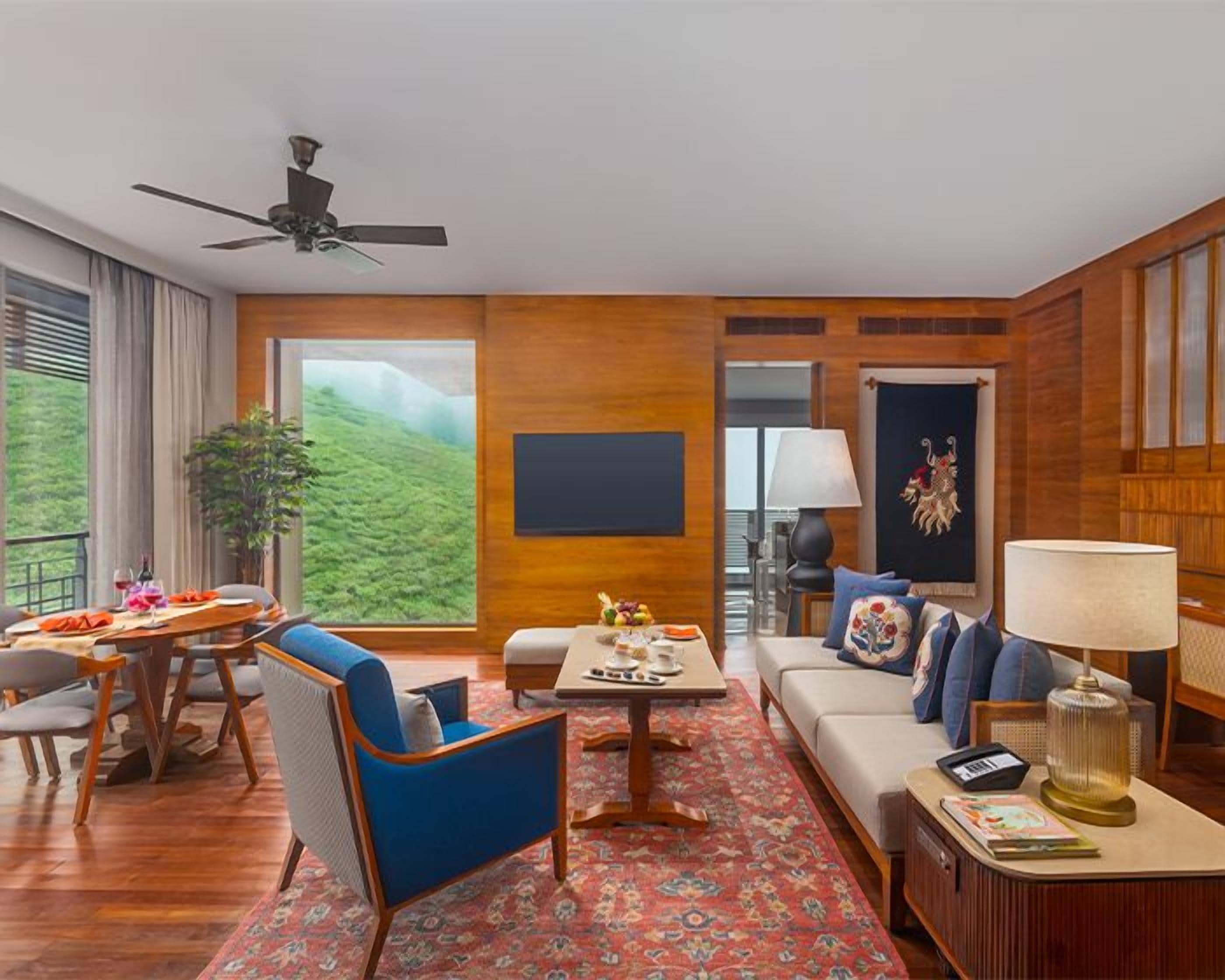A hotel room with a balcony, a sofa, a dining table, and a TV.