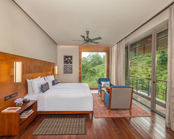Habitación de hotel con una cama grande, un escritorio, una silla, un balcón con vistas a zonas verdes y un ventilador de techo.