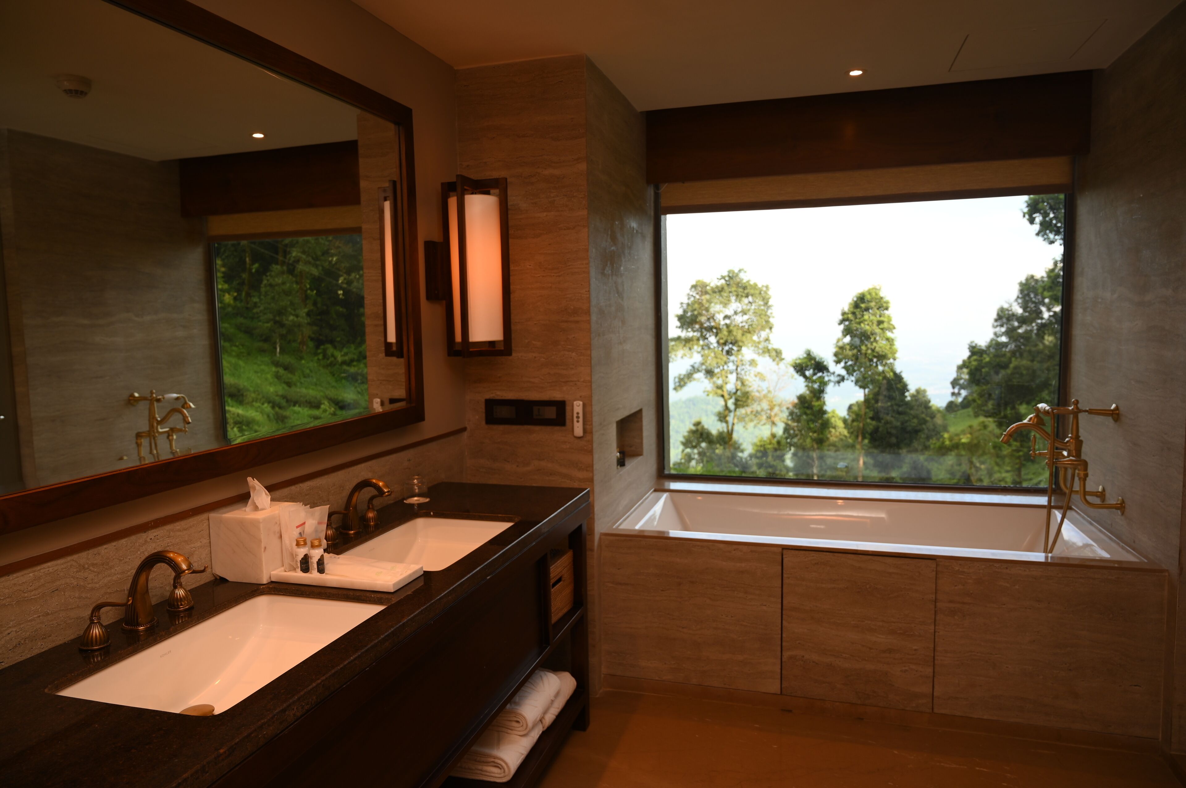 Un baño moderno con dos lavamanos, un espejo grande y una ventana con vistas a árboles.