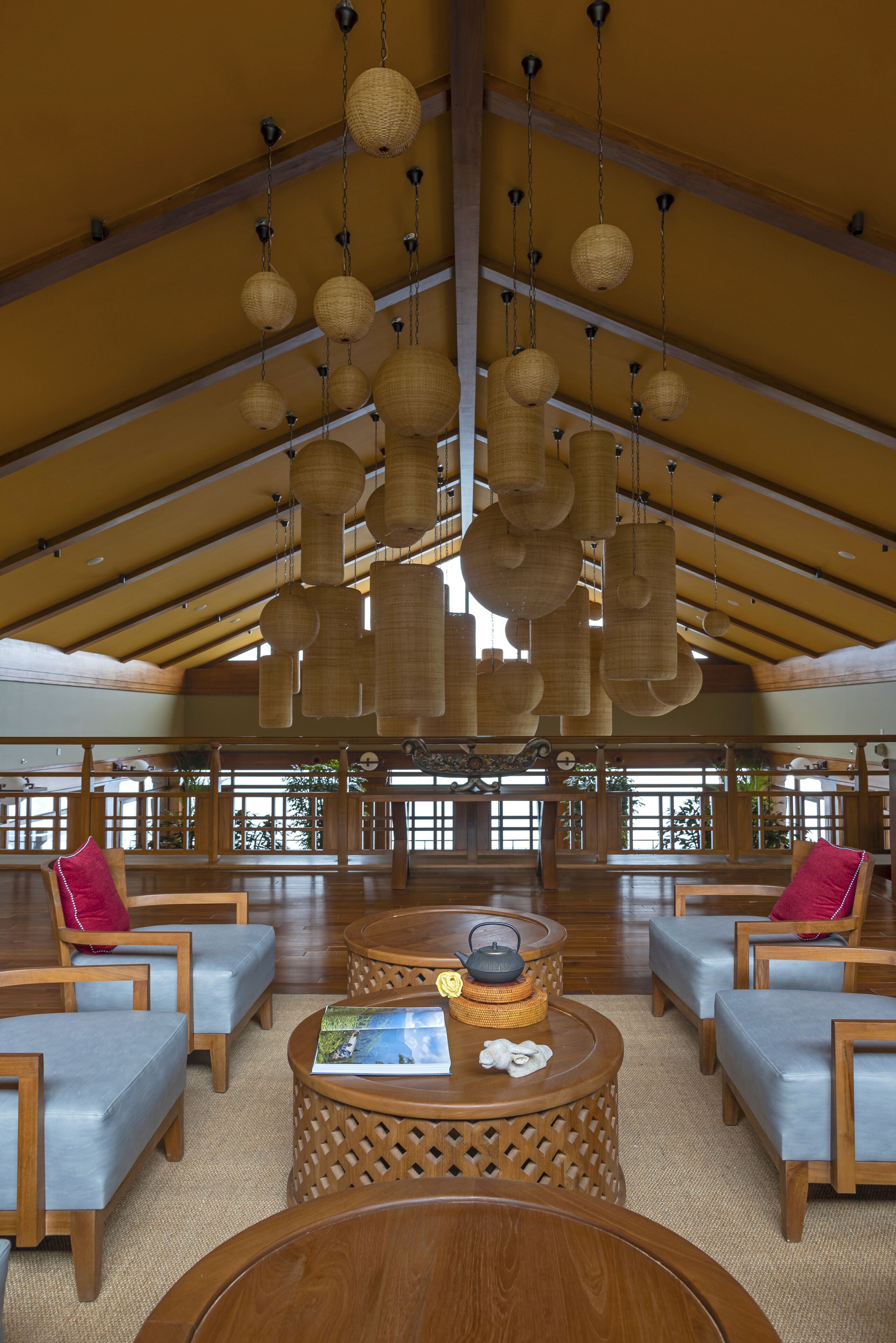Eine großzügige Lobby mit Holzmöbeln, einem runden Tisch in der Mitte und hängenden, gewebten Lampen.