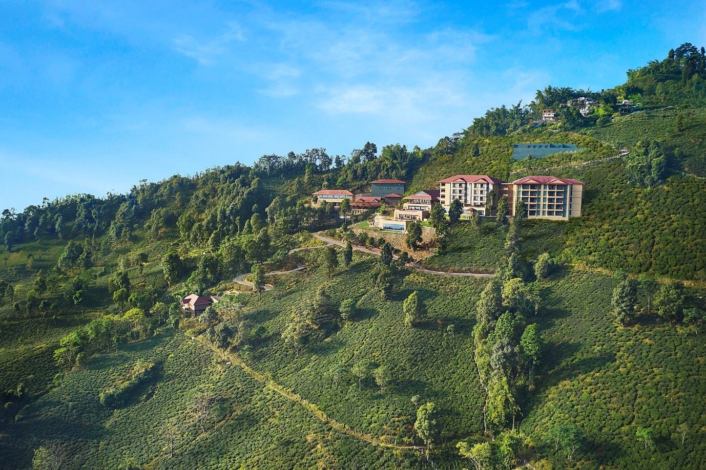 A hillside property with multiple buildings, including a large hotel with a red roof, surrounded by lush greenery and terraced fields.