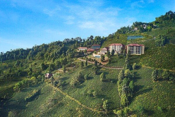 A hillside property with multiple buildings, including a large hotel with a red roof, surrounded by lush greenery and terraced fields. - Taj Chia Kutir Resort & Spa Darjeeling (Kurseong)