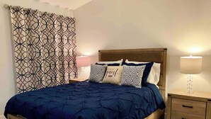 Ein Schlafzimmer mit einem hölzernen Bett, einem gemusterten Vorhang, einer Nachttischlampe und einem Nachttisch mit Lampe.