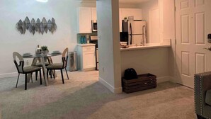 Ein kompakter Wohnraum mit Essbereich, Küchenzeile und einer Tür zu einem weiteren Zimmer.