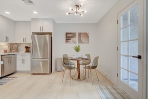Una cocina moderna con armarios blancos, electrodomésticos de acero inoxidable y un comedor con una mesa redonda y sillas.