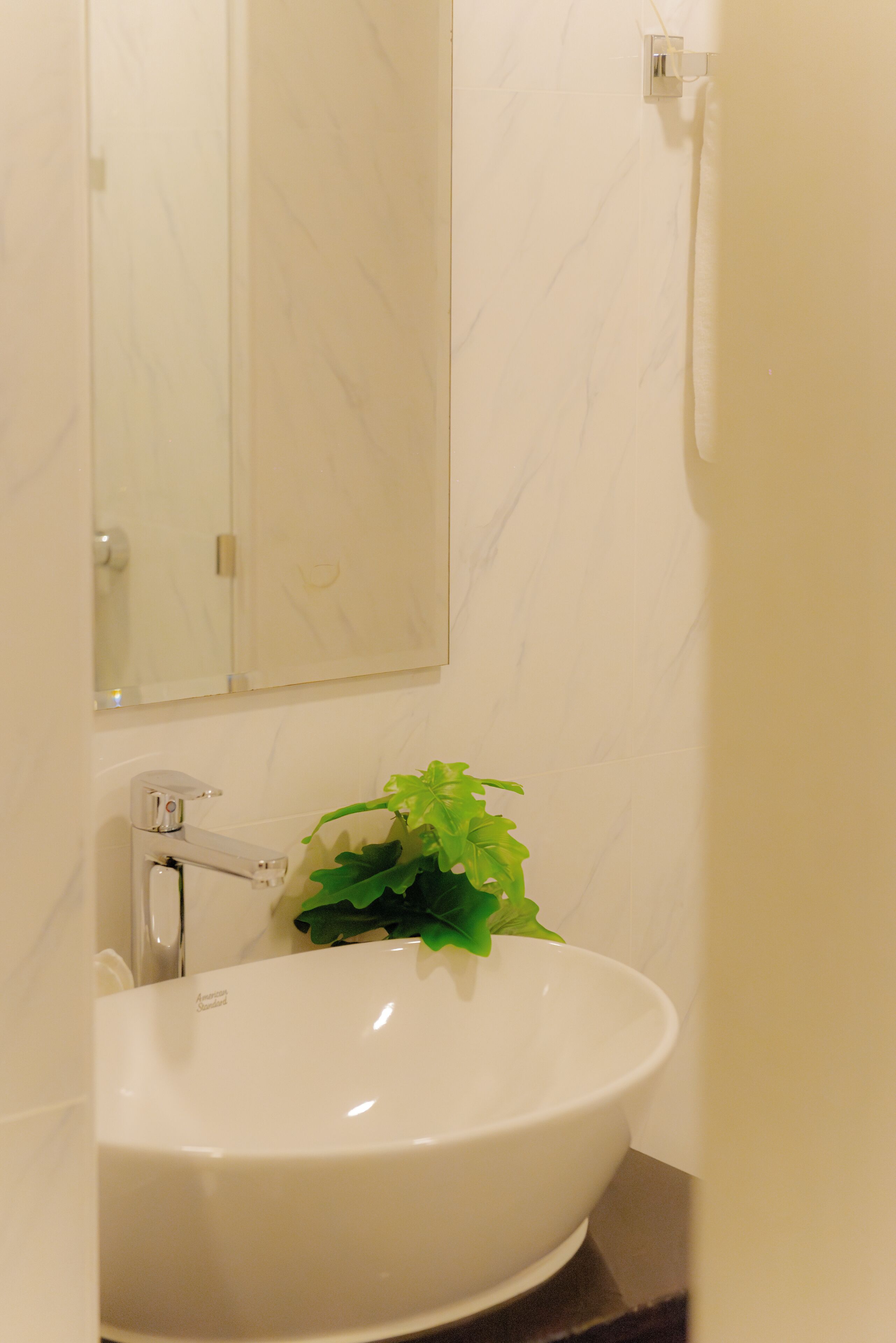 Une salle de bain avec un lavabo blanc, un miroir et une plante verte.