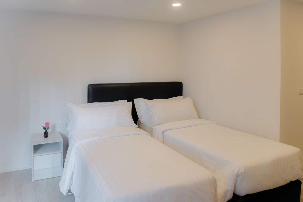 A double bed with white bedding in a room with white walls and a white nightstand.